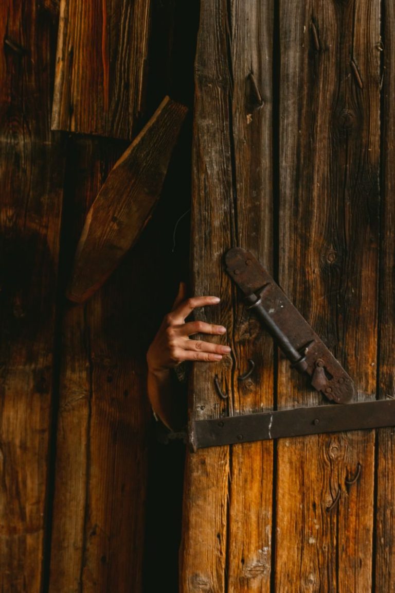 A hand reaching out from behind an aged wooden door evokes mystery and intrigue.